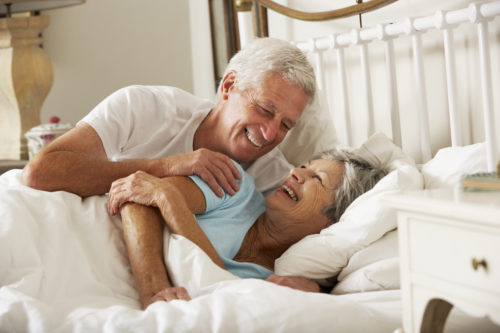 A man and woman laying in bed smiling for the camera.