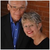 A man and woman laying in bed smiling for the camera.