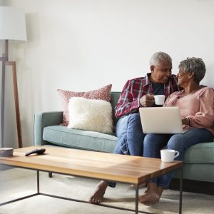 Senior Couple Sitting On Sofa At Home Using Laptop To Shop Online aging in place