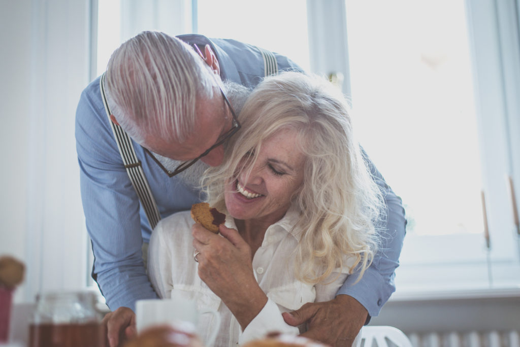 A man and woman laying in bed smiling for the camera.