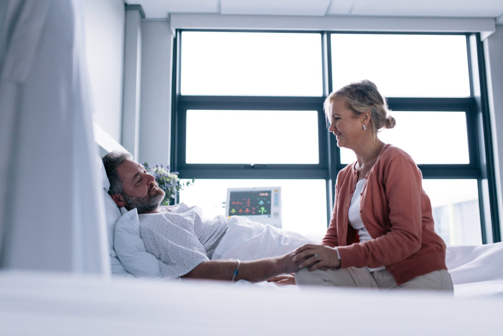 A man and woman laying in bed smiling for the camera.