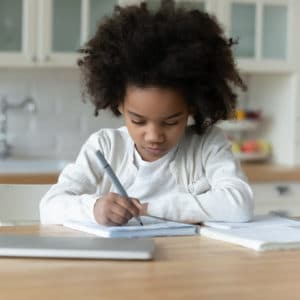 A young child is writing on paper at the table.
