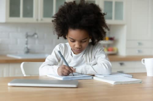 A young child is writing on paper at the table.