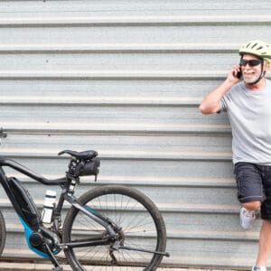 A man with a helmet on and a bicycle leaning against the wall.