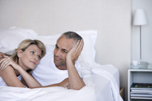 A man and woman laying in bed smiling for the camera.