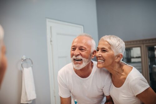 A man and woman laying in bed smiling for the camera.