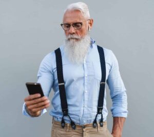 A man with long white beard and glasses looking at his phone.