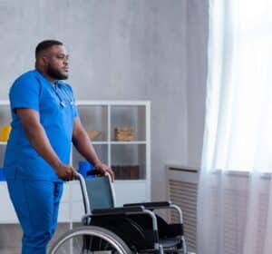 A man in blue scrubs pushing a wheelchair.