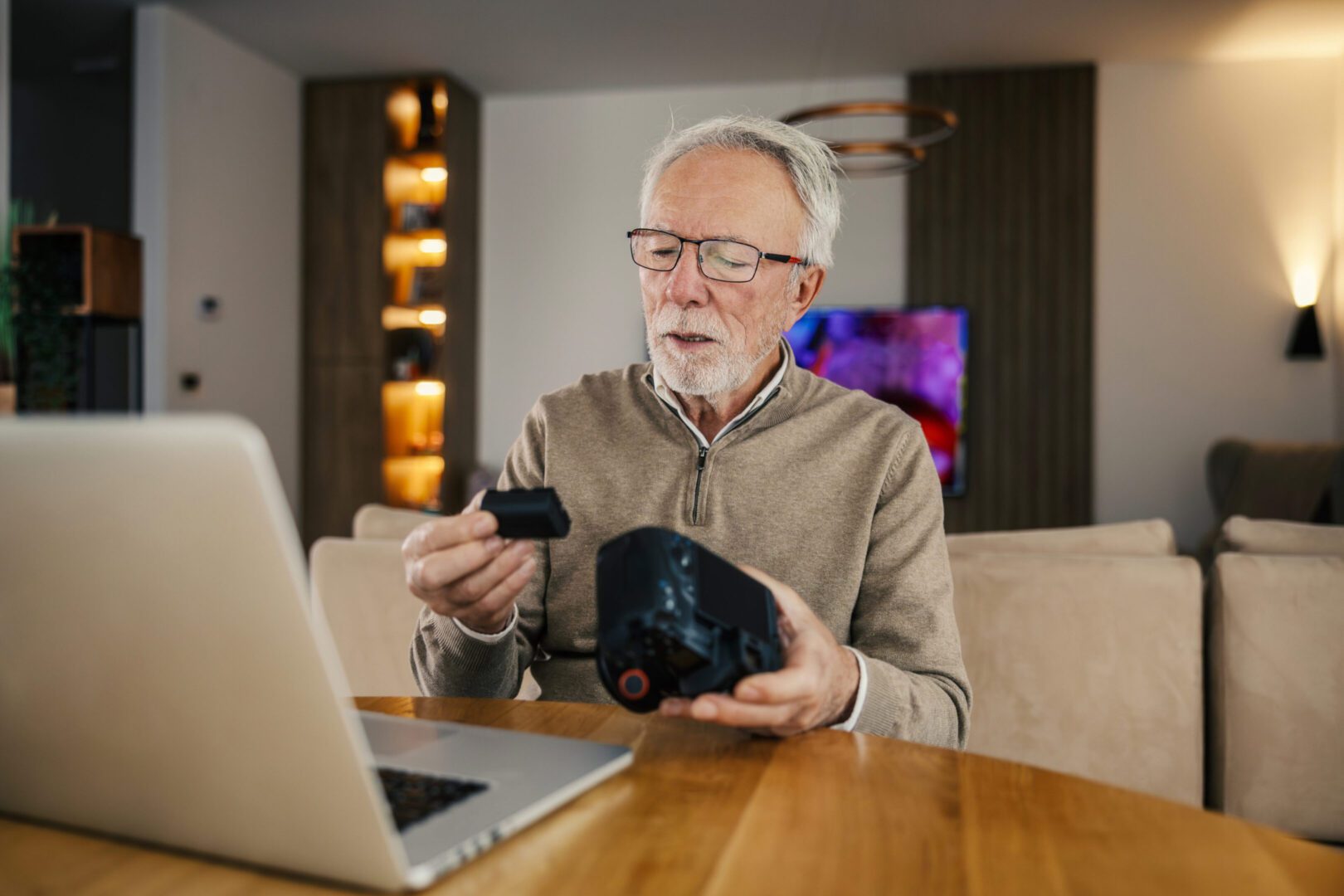 Senior inspecting camera beside laptop